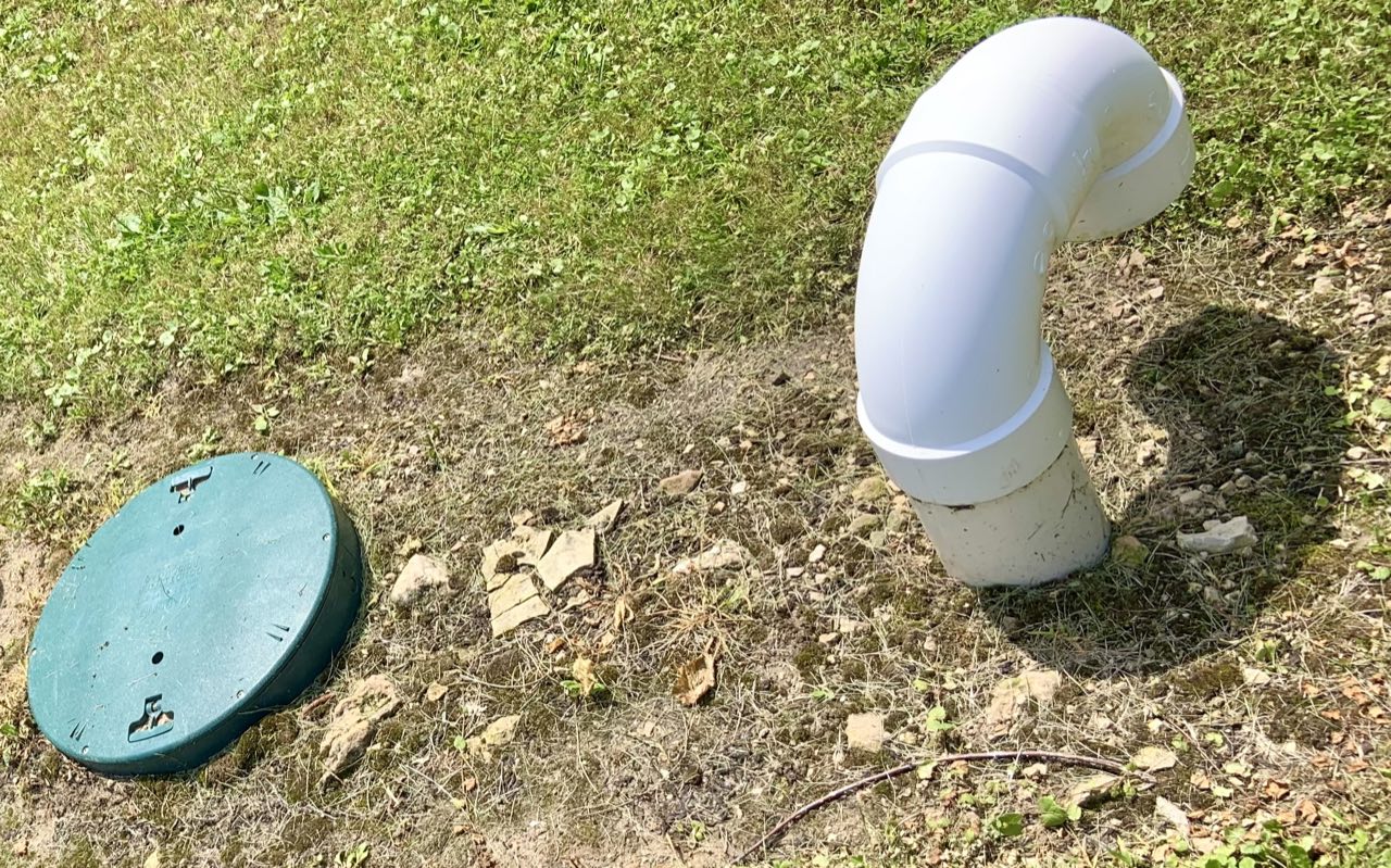 A green plastic septic riser lid and a white PVC vent pipe in a grassy yard.